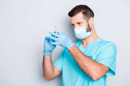 Portrait of busy serious medic with hairstyle in lab blue uniform and sterile mask checking,...