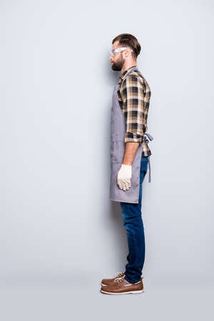 Full size body snap, half face side view portrait of attractive calm carpenter with hairstyle in safety glasses, jeans, isolated grey backgroundの写真素材