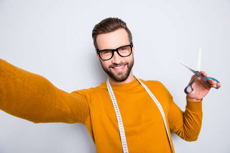 Self portrait of cheerful joyful attractive dressmaker shooting selfie on front camera holding scissors in hand and centimeter on neck, having fun leisure video-call, isolated on grey backgroundの写真素材