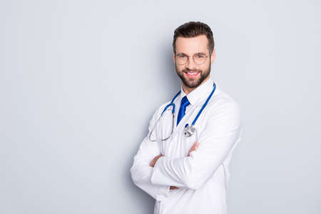Portrait with copy space of cheerful joyful doc with bristle in white lab coat and stethoscope on his neck, having his arms crossed, looking at camera, isolated on grey backgroundの写真素材