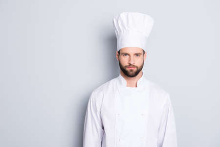 Portrait of strict confident chef cook with stubble in beret and white outfit looking at camera isolated on grey backgroundの写真素材