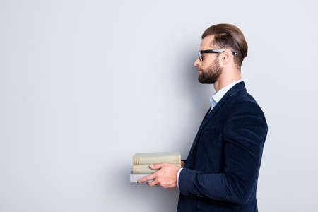 Profile side view half face portrait with copyspace, empty place of calm concentrated teacher in shirt, jacket with stubble having three books in hands, isolated on grey backgroundの写真素材