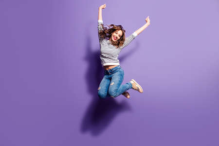 Portrait of cheerful positive girl jumping in the air with raised fists looking at camera isolated on violet background. Life people energy concept