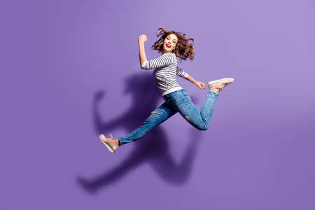 Portrait of sportive active girl in motion jumping over in the air isolated on violet background...