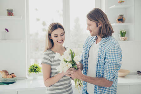 Portrait of trendy stylish couple enjoying holiday together, handsome man giving bouquet of white tulips to lover making surprise. Daydream delight lovestory conceptの写真素材