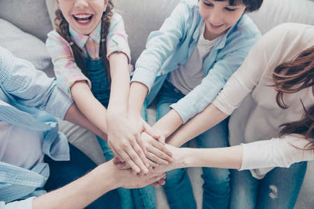 Top view cropped portrait of family with two kids sitting on sofa indoor putting hands on top of...