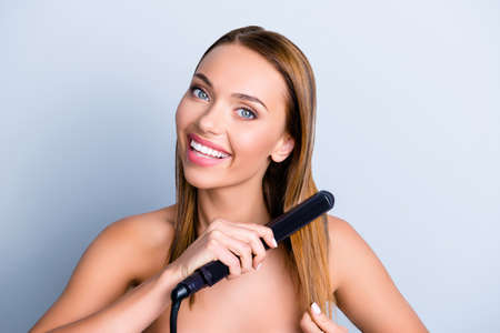 Hand shiny silky smooth curls wavy make prepare design tool temperature ceramic wet bathroom concept. Close up portrait of beautiful cute girl holding hot iron in hand isolated on gray backgroundの写真素材