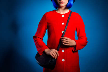 Cropped portrait of fashionable pretty woman in red outfit with black bag on shoulder isolated in bright blue background. Wear cloth conceptの写真素材