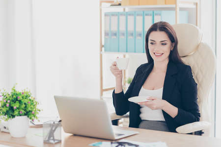 Portrait of cheerful charming woman having coffee break watching film video movie sitting at desk in...