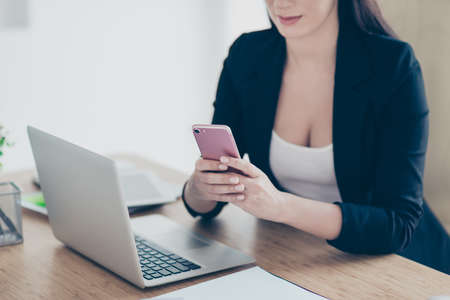 Cropped portrait of tempting seductive woman holding smart phone having break pause chatting with friends checking email using wifi 5G internet sitting at desk in work placeの写真素材