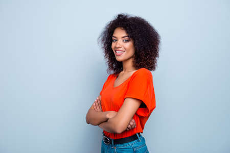 Portrait of joyful cute woman with plump lips modern hairdo in orange t-shirt holding hands crossed...