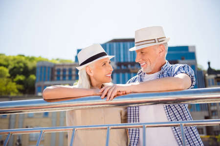 Portrait of beautiful romantic grandma and granddad in straw hats enjoying walk together looking at each other having pleasure sunny day. Rest relax weekend vacation holiday conceptの写真素材
