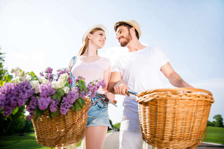 Low angle view portrait of lovely romantic couple in casual outfits riding on bikes looking at each other. Sunlight sun sunshine weather love story idyllic daydream conceptの写真素材