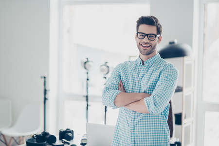 Portrait of attractive cheerful photo camera lover standing in  photo studio with crossed arms, laughing at camera, his hobby to shoot nice photo sessionsの写真素材