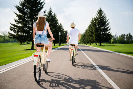 Rear view portrait of two sportive carefree traveler riding on bikes in park. Healthy lifestyle sunny day adventure pursuit vitality concept, enjoying sunshine sunlightの写真素材