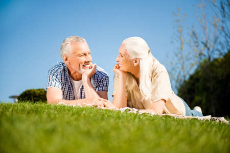 Portrait of cheerful positive spouses lying on blanket on lawn looking at each other enjoying...