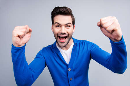 Close up portrait of emotional, cheerful, funny guy with raised arms, celebrating a victory of his favorite sport team, isolated on grey backgroundの写真素材