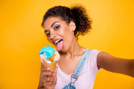 Self portrait of tempting seductive girl having vanilla ice cream in waffle cone licking with tongue...