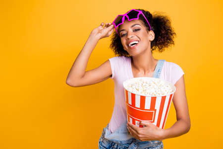 Portrait with copyspace of cheerful positive laughter looking out star glasses holding big bucket of pop-corn enjoying new comedy isolated on yellow backgroundの写真素材