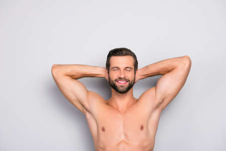 Attractive, stunning, manly, smiling macho isolated on gray background, having two arms behind the head and closed eyes, showing his shaven armpits - wellness, wellbeing conceptの写真素材
