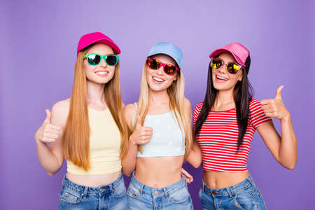 Portrait of cheerful positive trio with beaming smiles gesturing thumb up signs isolated on bright violet background. Advertisement conceptの写真素材