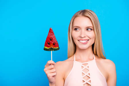 Portrait of funny excited girl looking at sweet tasty piece of watermelon on stick biting low lip...