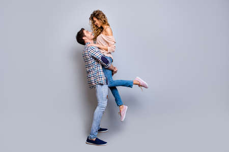 Profile full body portrait of lovely romantic couple, strong man holding charming woman looking at...