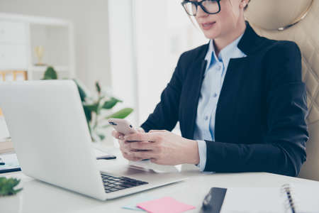 Cropped portrait of serious concentrated expert in shirt jacket typing sms holding smart phone in hands using 3G wi-fi internet sitting in modern workstationの写真素材