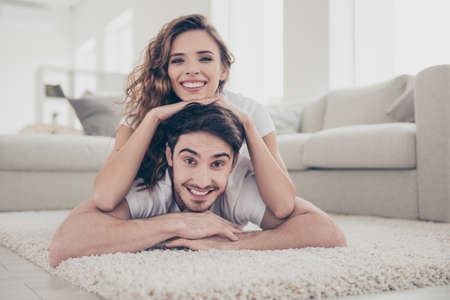 Portrait of positive cheerful couple lying on floor, woman on top of lover looking at camera having beaming smiles modern hairstyle. Weekend holiday conceptの写真素材