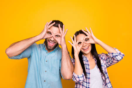 Portrait of funky cheerful couple making binoculars with fingers wearing casual shirts isolated on...
