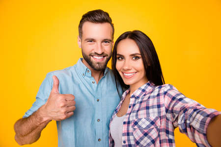 Self portrait of stylish trendy couple embracing showing like sign shooting selfie on front camera...