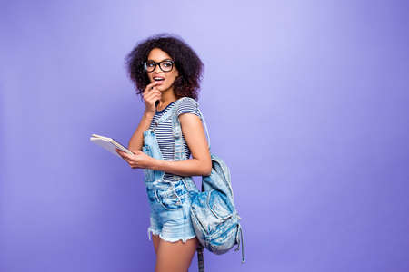 Portrait with copy-space of thoughtful pensive girl in jumpsuit with backpack holding notebook in...
