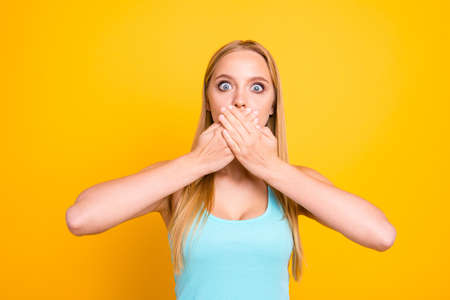 Close up portrait of pretty cute terrified frightened girl with mute dumb silent and palms over mouth isolated yellow background. Concept of advertisingの写真素材