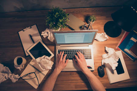 Top view portrait of man's hands typing on keypad of laptop, having crumpled drafts, tablet, smart...