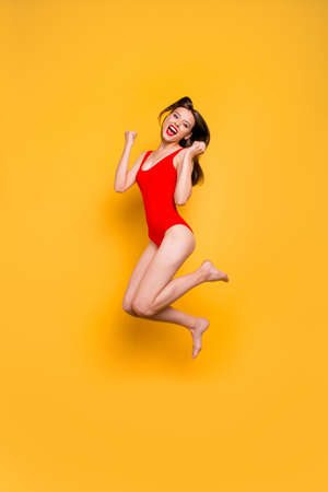Finally, holidays! Full-legs vertical portrait of girl jumping clenching her hands in fists and joyfully screaming isolated on yellow backgroundの写真素材