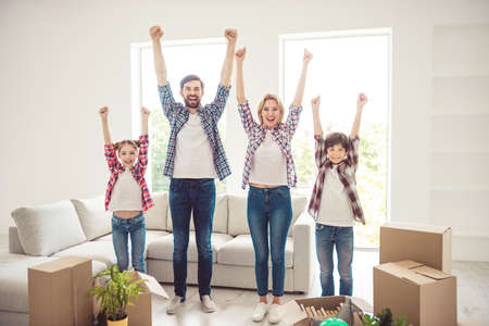 Success concept. Young happy smiling caucasian family wearing casual moving to new flat, standing toghether raising hands up in light living roomの写真素材