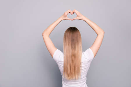 Portrait from the back of charming blond girl holding hands over her head and showing a heart isolated on gray backgroundの写真素材