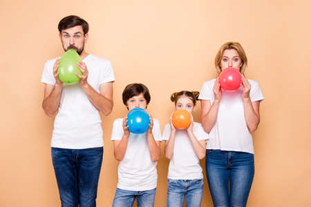 Young family, bearded father, blonde mother, boy and girl wearing blue jeans and white T-shirts, blowing air balls green beige red blueの写真素材