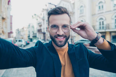 Self portrait of cheerful joyful man shooting selfie on front camera while walking over street...