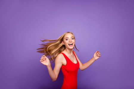 Portrait of attractive excited blonde gorgeous girl wearing red swim suit with opened mouth, wind blows hair, motion. Isolated over violet pastel backgroundの写真素材