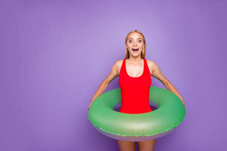 Water is so warm! Photo portrait of charming joyful rejoicing cute lovely girl holding lifebuoy on waist in hands looking at camera isolated on violet background copy spaceの写真素材