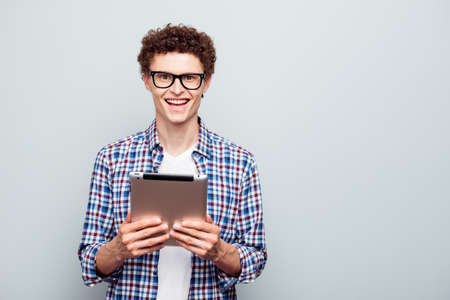 Portrait of happy clever young student man holding digital tablet in hands isolated on gray background with copy space for textの写真素材
