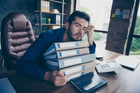 Tired man holds a telephone receiver in his hand wrapped in a cord and looking straight into the...