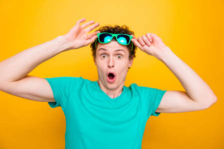 Young attractive handsome shocked guy wearing casual green polo t-shirt and sun glasses, raising...