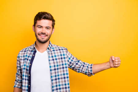 Portrait of handsome young man standing isolated on bright yellow background and holding something in his outstretched fistの写真素材
