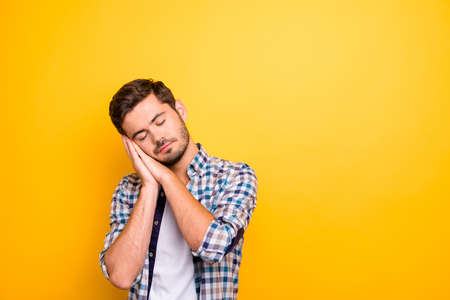 Close up portrait of young brunet folded his arms under his head pretending to be sweetly asleep isolated on vivid yellow background with copy space for textの写真素材
