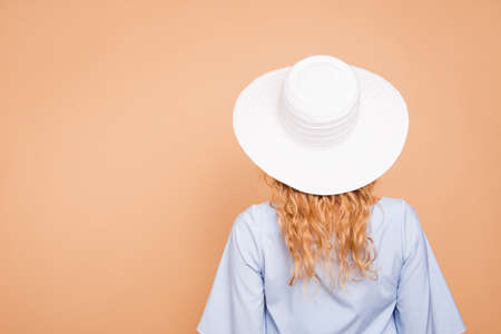 Back behind rear view of young attractive caucasian curly-haired gorgeous woman wearing sunhat and blue dress. Isolated over pastel yellow background, copy spaceの写真素材