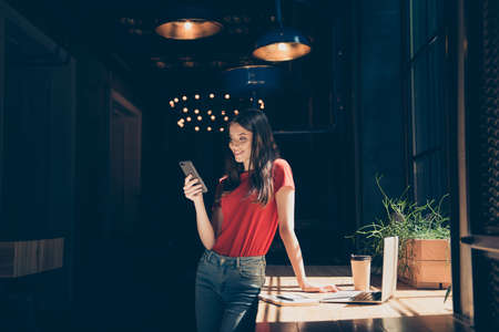 Attractive nice smiling young girl freelancer student wearing casual in cafeteria, working remotely, reading sms, dark interiorの写真素材