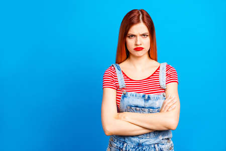 Red straight-haired vivid young girl with folded hands, wearing casual, isolated over blue...