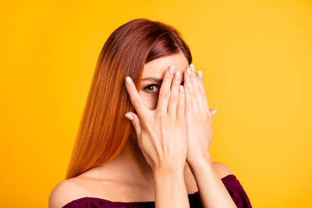 Portrait of cheerful and sweet girl close her eyes with palms, peeking out open fingers on one hand, isolated on yellow backgroundの写真素材